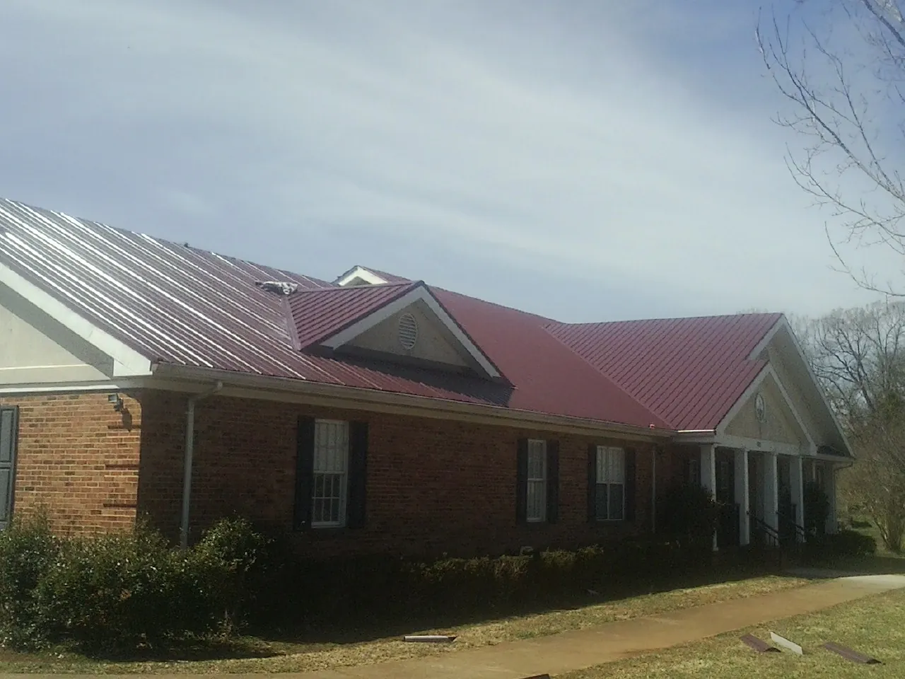 Red metal roof with gabled entries on a long brick building, from a Hail Damage Roof Repair job in Riley