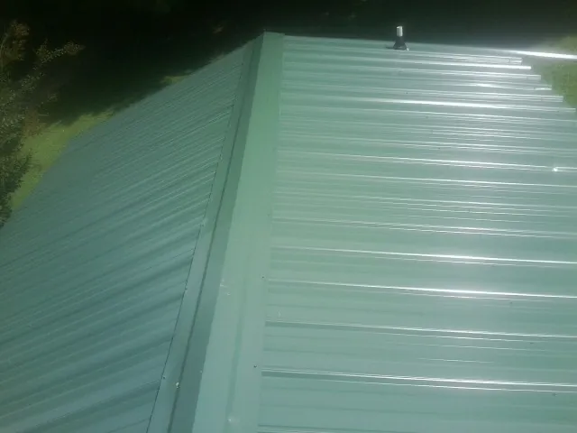 New green metal panels meeting at the ridge of a roof — Flat Roof Repair work by our crew in Riley