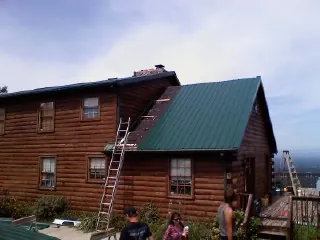 Green metal roof going on a two story log home with ladders set in Riley