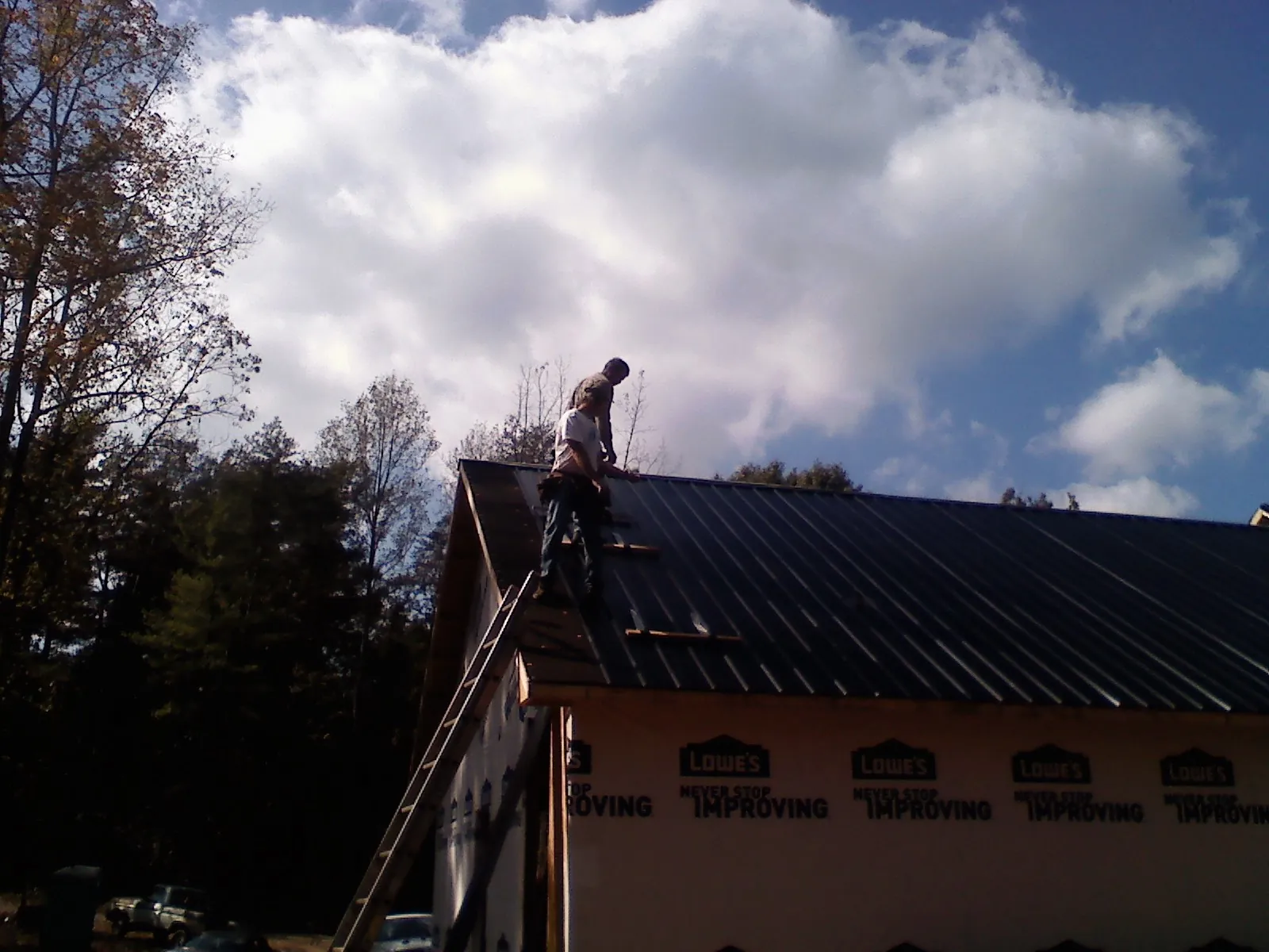 Roofer fastening dark metal panels high against a cloudy sky, from a Roof Inspection job in Riley