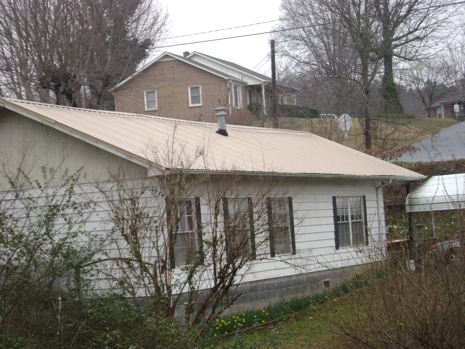 Tan metal roof on a white sided house set into a hillside — Commercial Roofing by Roofing Brothers in Riley