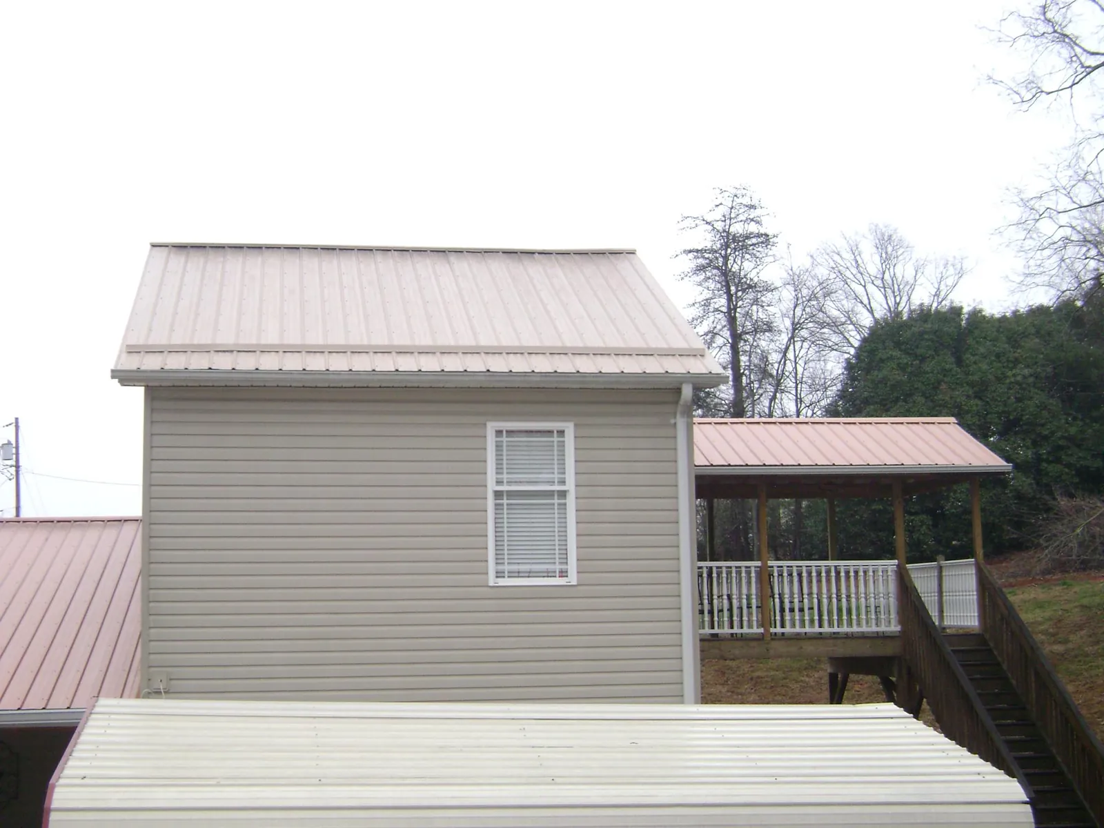 Tan metal roofs on a two story addition and attached porch, from a Roof Replacement job in Riley